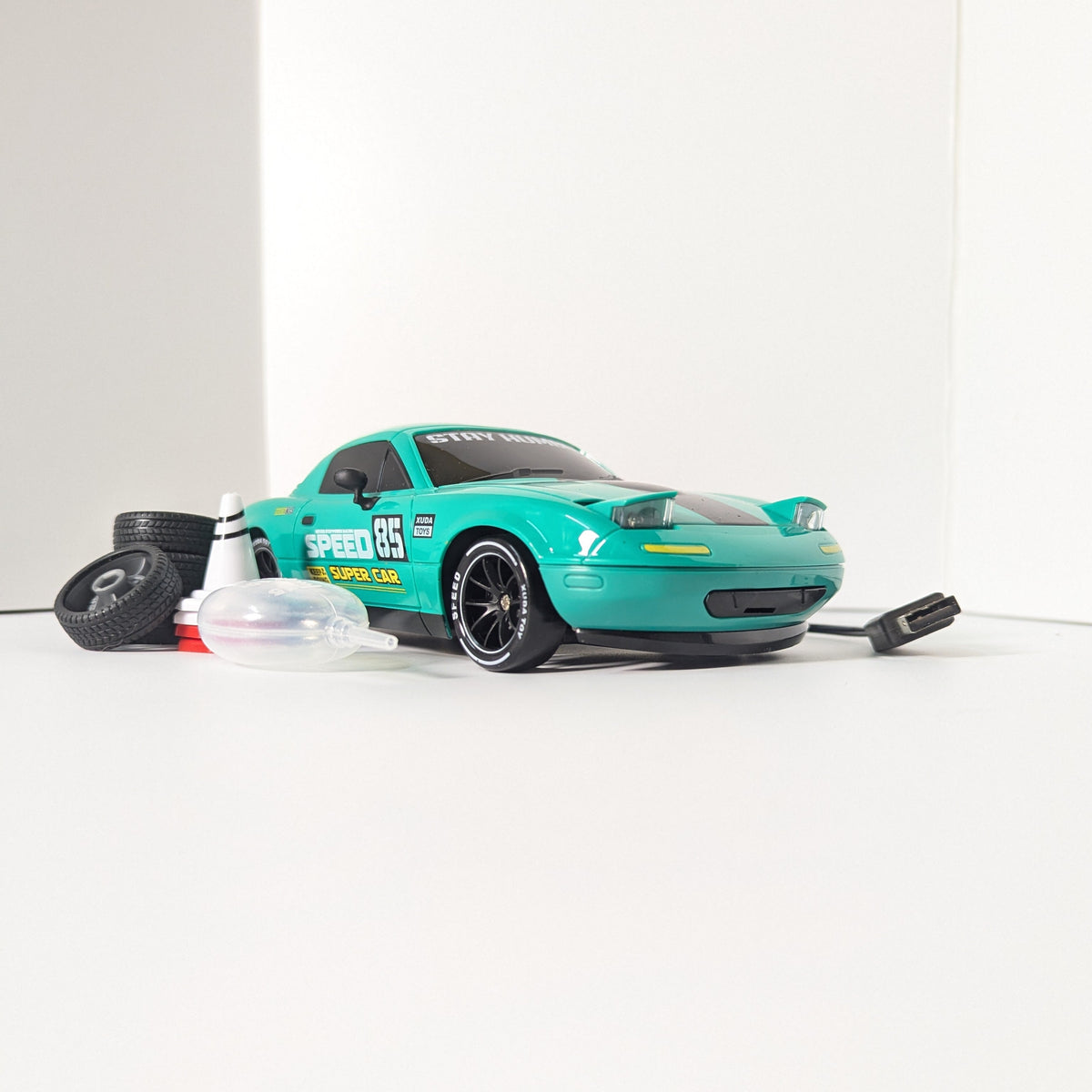 A turquoise and black remote control drift car with racing decals, displayed on a clean white background with its tires and accessories.